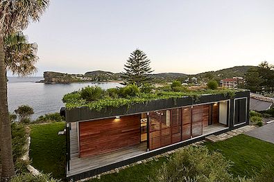 Een groen, geprefabriceerd huis met een uitzicht op de woonkamer en het water